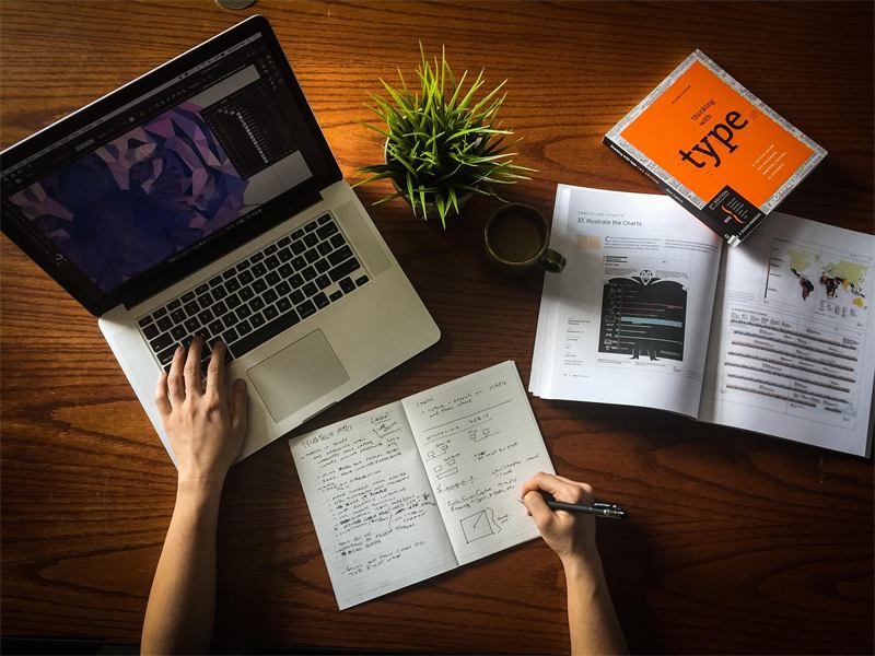 Designer sketching beside a laptop and a typography book