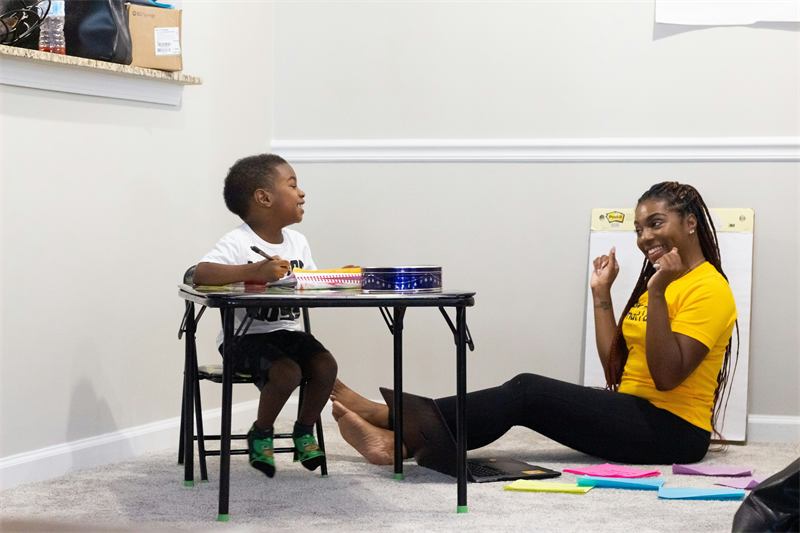 Tutor teaching a young boy at a small desk at home